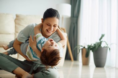 Playful mother having fun with her small son at home.