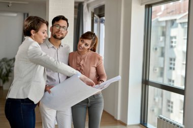 Young couple analyzing housing plans with real estate agent while buying new home. 
