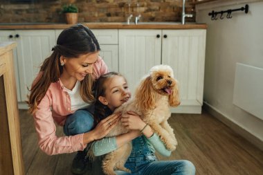 Happy little girl and her mother enjoying with their dog at home. 