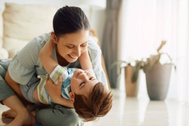 Young happy mother having fun while playing with her small son at home.