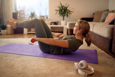 Athletic woman using hand weights while doing sit-ups in the living room.