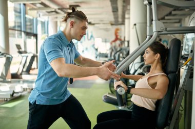 Genç sporcu kadın vücut gücünü arttırmak için egzersiz yapıyor. Bu sırada antrenörü ona spor salonunda yardım ediyor.. 