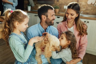 Happy parents and their small daughters having fun with a dog at home. 