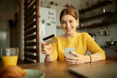 Happy woman shopping online with credit card and mobile phone at home. 