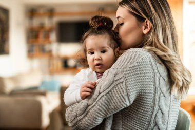 Loving mother showing affection to her small daughter and kissing her at home. 
