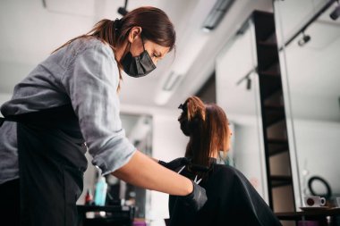 Hairdresser cutting customer's hair and wearing face mask due to coronavirus pandemic.