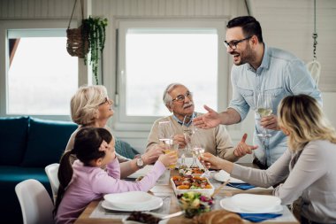 Happy man talking to his family while proposing a toast during lunch at dining table. 