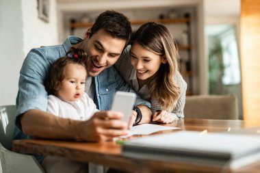 Young parents having fun while taking selfie with their small daughter at home. 