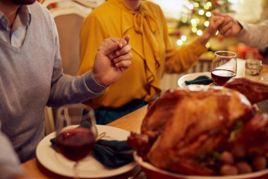 Close-up of family holding hands and praying before a meal on Christmas at dining table.