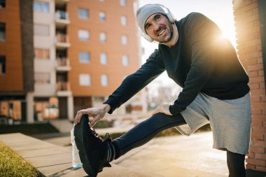 Young happy sportsman warming up while doing stretching exercises on the street.