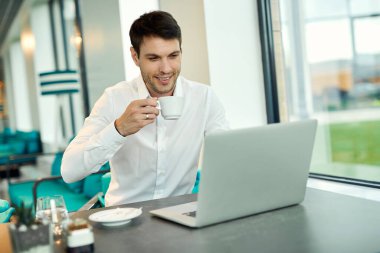 Happy businessman working on a computer while drinking coffee in a cafe. 