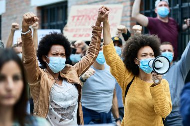 African American woman wearing protective face masks and holding hands while participating in demonstrations for human rights on the streets. 