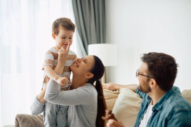 Happy parents having fun with their small son at home. Focus is on mother touching son's nose.