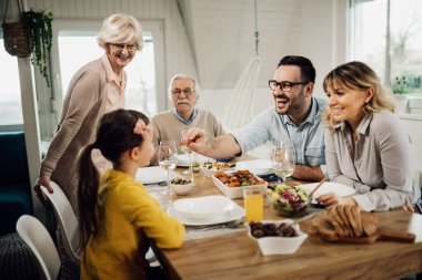 Happy extended family enjoying lunch at dining table while father is feeding daughter. 