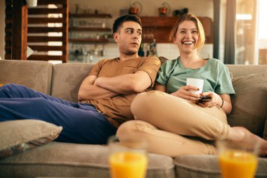 Young woman laughing while watching TV with her boyfriend at home. 