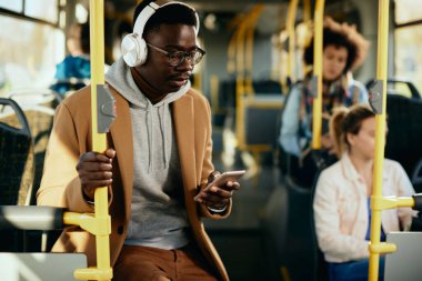 African American man using mobile phone and listening music over headphones while commuting by public transport. 