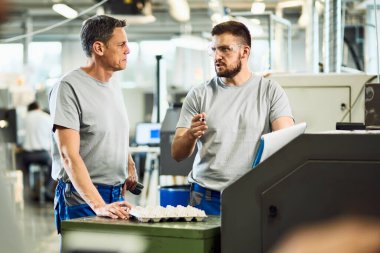 Two manual workers talking while working in a industrial facility. 