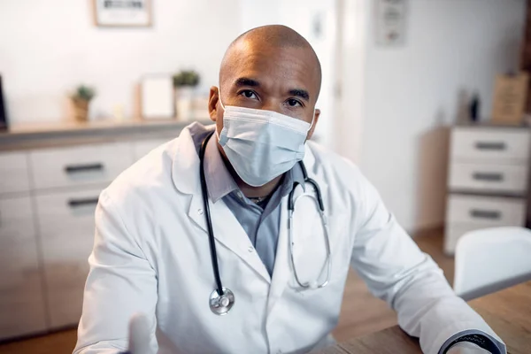 Black doctor working at the clinic during coronavirus pandemic and wearing a face mask while looking at camera.