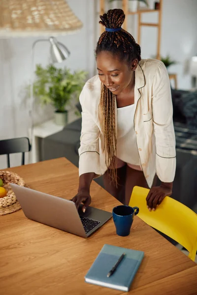 Young happy black woman surfing the net on laptop at home.