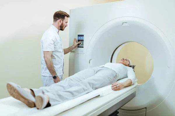 Medical technician and mature patient during MRI scanning procedure at clinic.