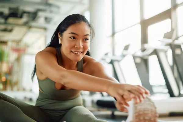 Young Asian athletic woman warming up and doing stretching exercises in a gym.