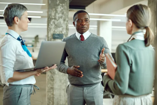 Black executive director communicating with female members of his business team during the briefing in the office.