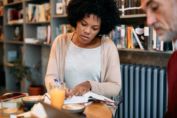 Mid adult African American woman doing some research with her mature friend while studying together in a library.