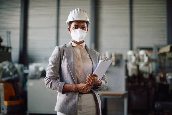 Black female engineer with face mask standing at distribution warehouse and looking at camera.
