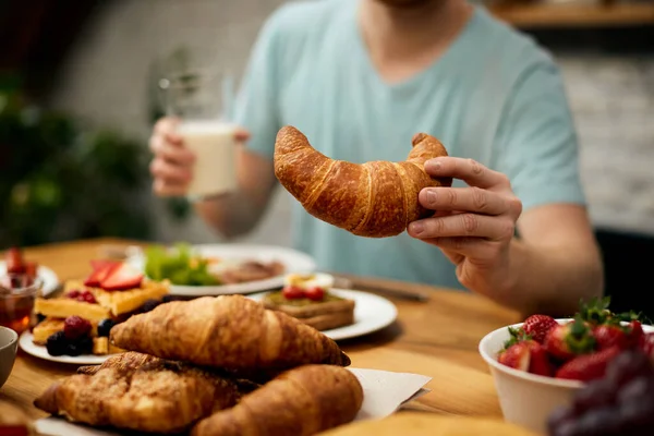 Close-up of man eating croissant for breakfast at home.