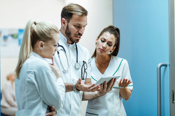Male doctor and nurses communicating while working on digital tablet at clinic. 