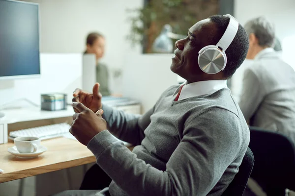 Black businessman taking a break from work and listening music over headphones at his office desk.