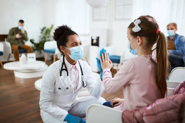 African American female dentist giving high-five to a little girl at dental clinic during COVID-19 pandemic.