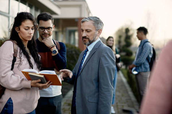 University students and their professor going through lecture while standing outdoors at campus. 
