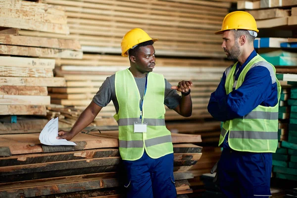 African American worker and his colleague talking while making delivery plans at wood distribution warehouse.