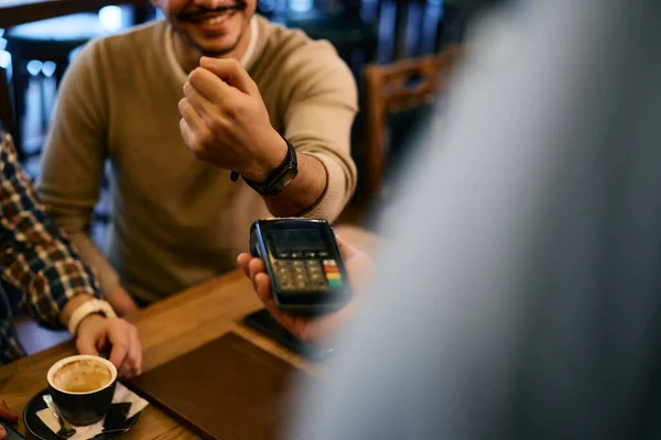 Close-up of male guest paying to a waiter via contactless smart watch app.