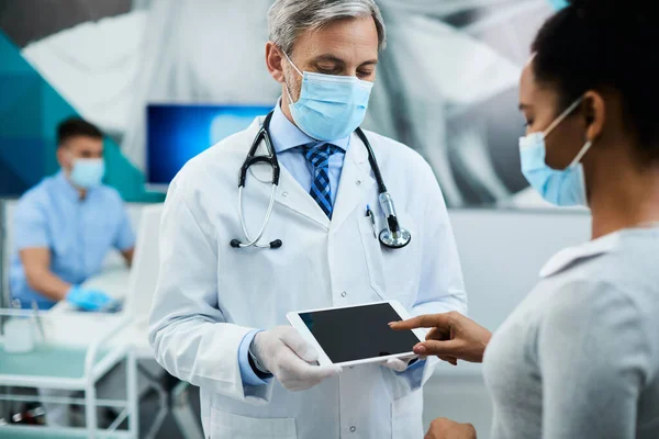 Black woman signing on touchscreen of digital tablet while having appointment with her dentist at dental clinic. Focus is on dentist.