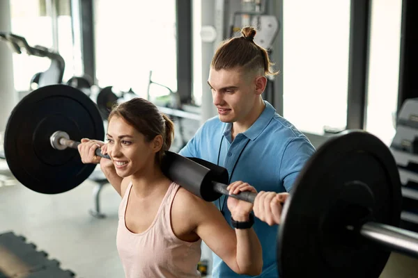 Male coach assisting sportswoman while she is exercising with barbell in a gym.