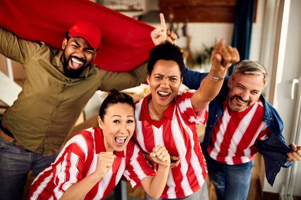 Multi-ethnic group of people cheering for their team while watching sports match on TV at home.