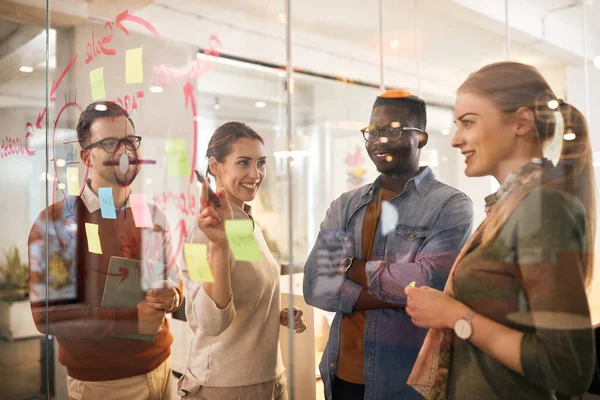 Happy creative entrepreneurs working on new business strategy and writing ideas on a glass wall during the meeting.