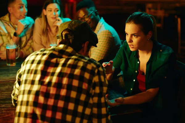 Young woman having an argument with her boyfriend while being on night date in a pub. Their friends are in the background.