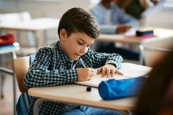 Schoolboy writing in notebook during a class at school.