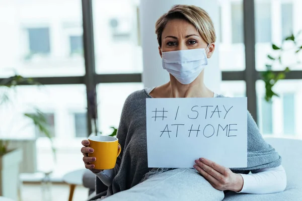 Happy woman wearing face mask and holding placard with hashtag I stay at home.