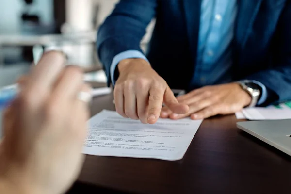 Close-up of insurance agent closing a deal with a client and pointing at place of signature.