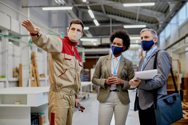Company managers communicating with male worker while visiting factory facility during coronavirus pandemic.