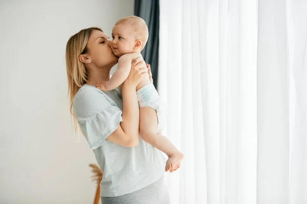 Young Affectionate Mother Holding Her Baby Boy Kissing Him Home — Fotografia de Stock