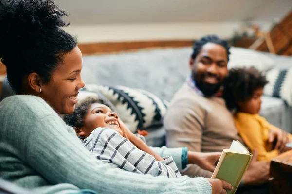 Happy African American mother having fun while reading a story to her son at home.