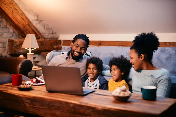 Happy black parents and their kids watching something on laptop while relaxing together at home.