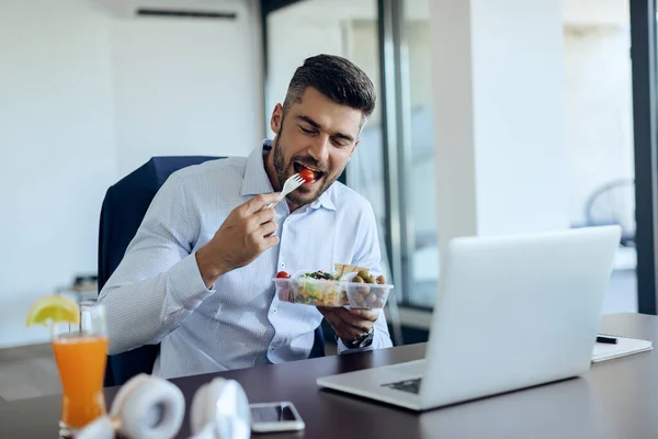 Young businessman taking a break from work and eating healthy food for lunch in the office.