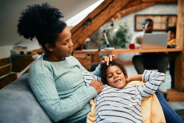 Happy African American mother enjoying with her son while he is relaxing on her lap at home.