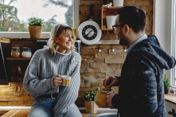 Happy woman having a cup of tea and talking to her husband in the kitchen.